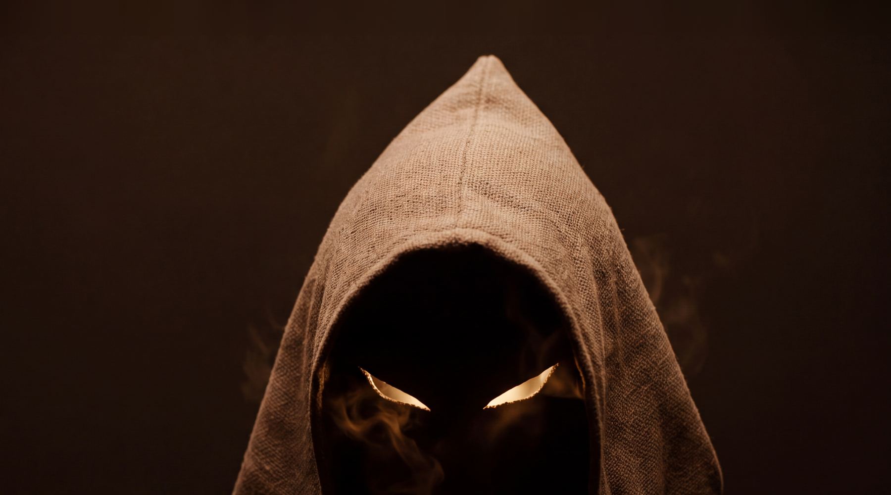 The Watcher: a hooded figure in sackcloth, its eyes two slits of ember light. Poncho's mascot.